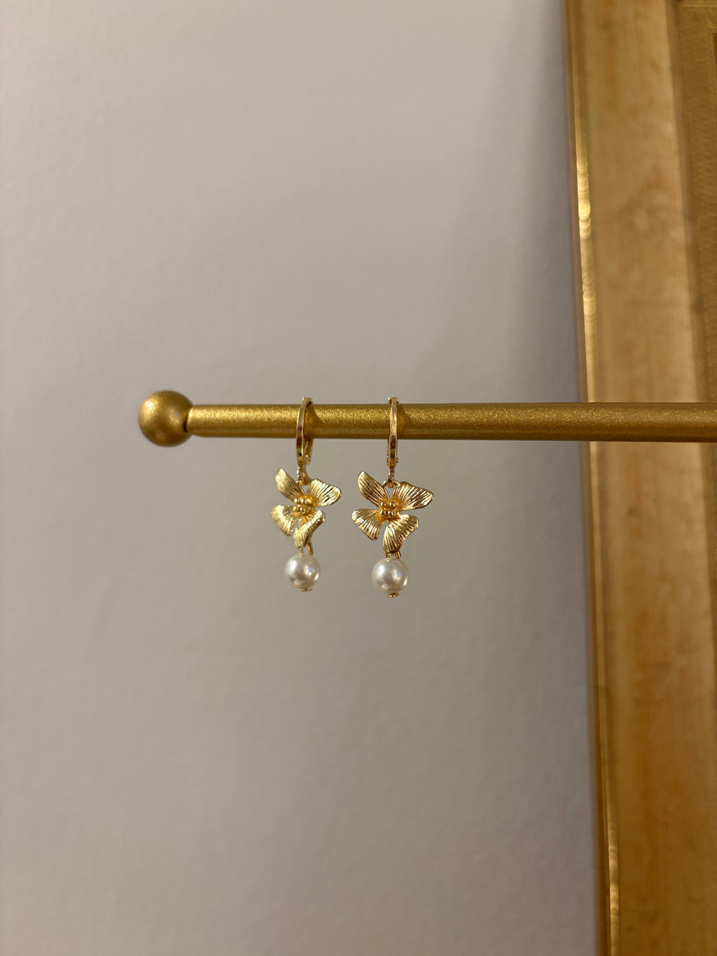 Gold earrings with angel designs and pearl drops on a gold stand against a neutral background