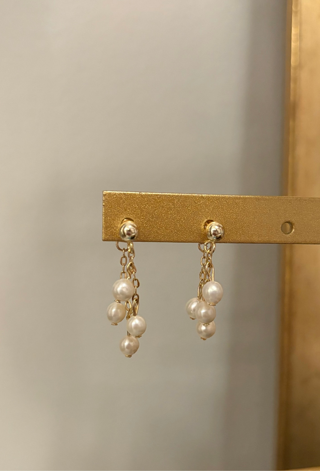 Pearl earrings hanging on a gold bar against a neutral background