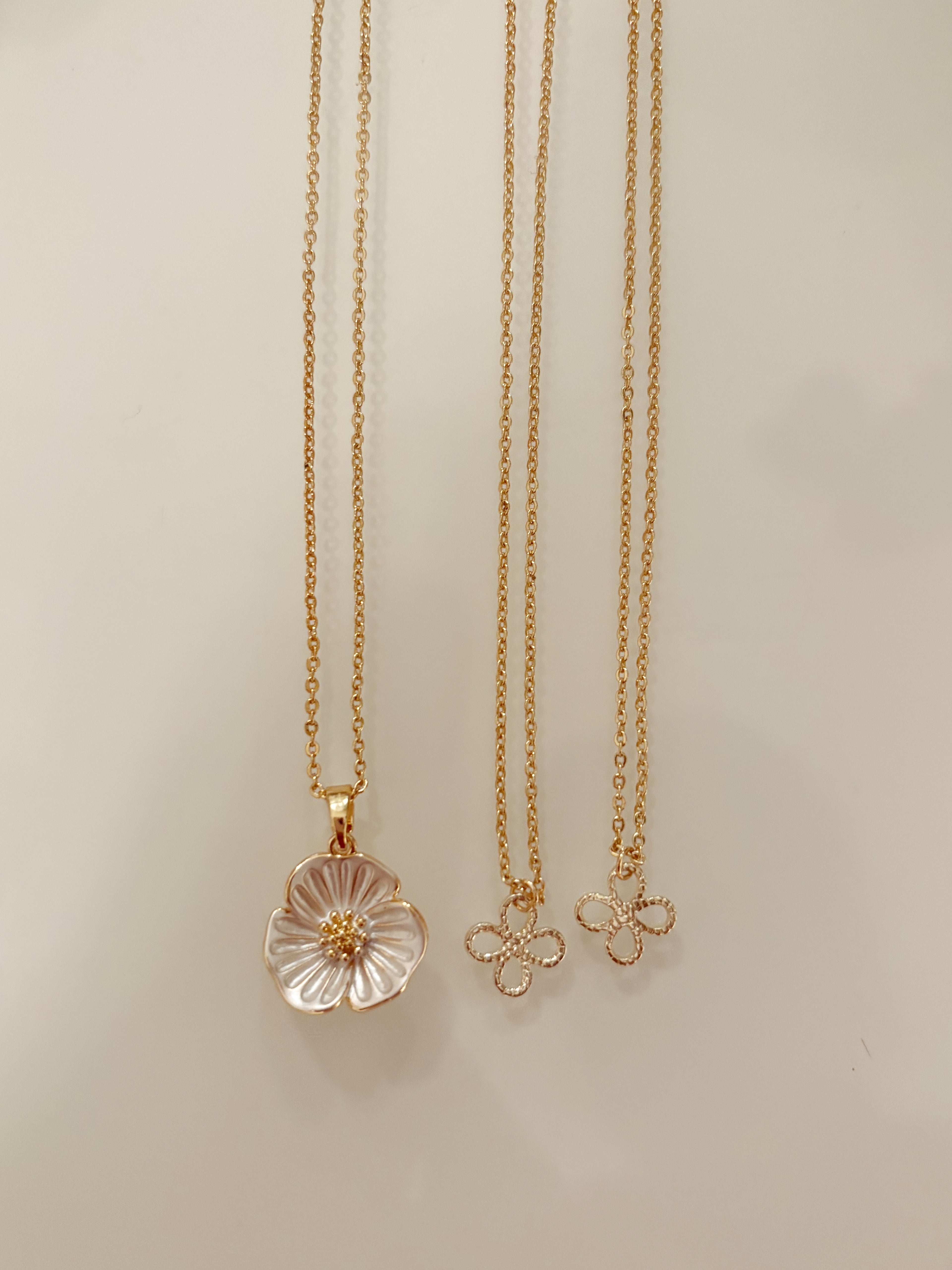 Two gold necklaces with floral pendants on a light beige background