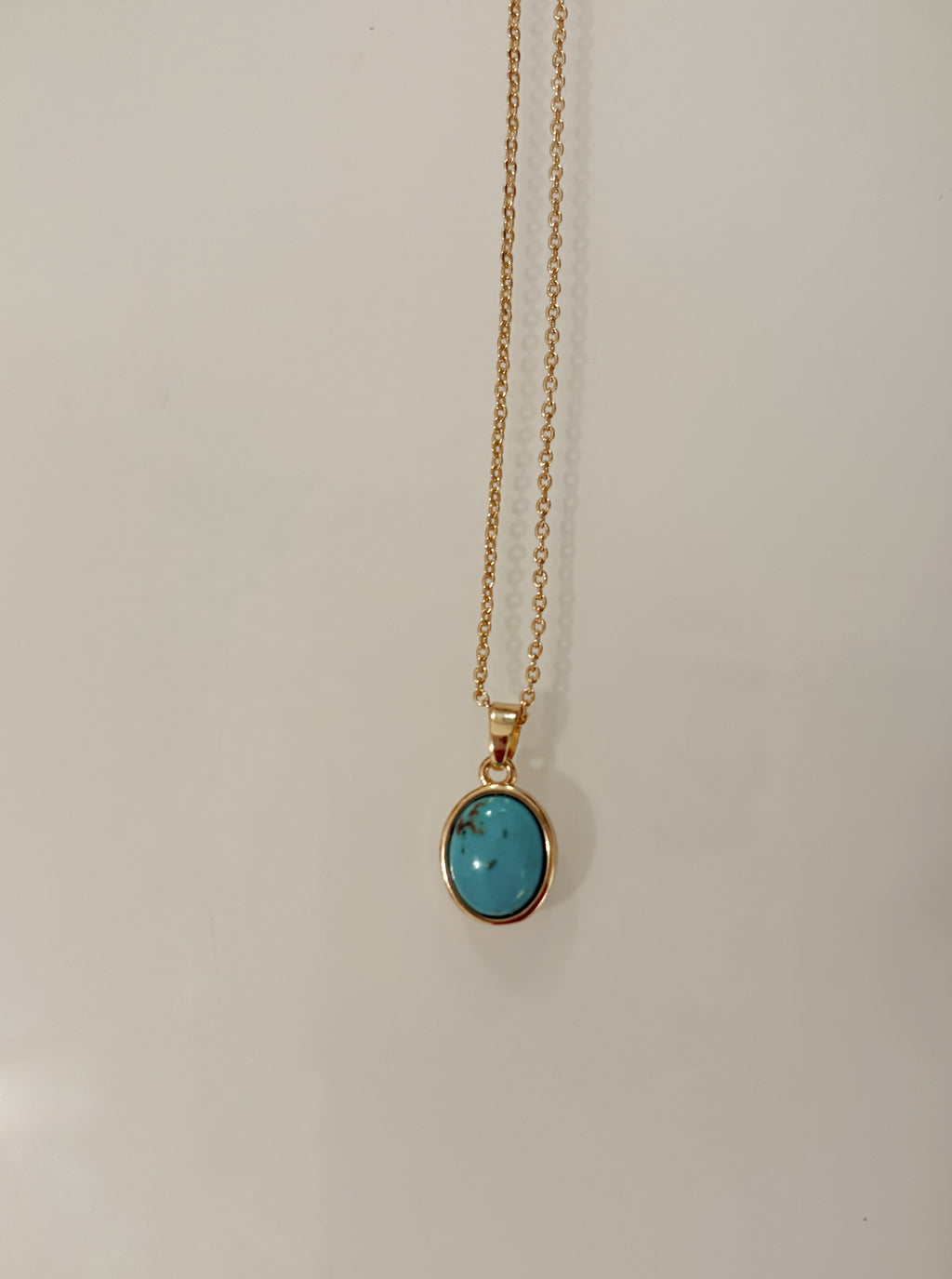 Gold filled necklace with a turquoise pendant on a light gray background