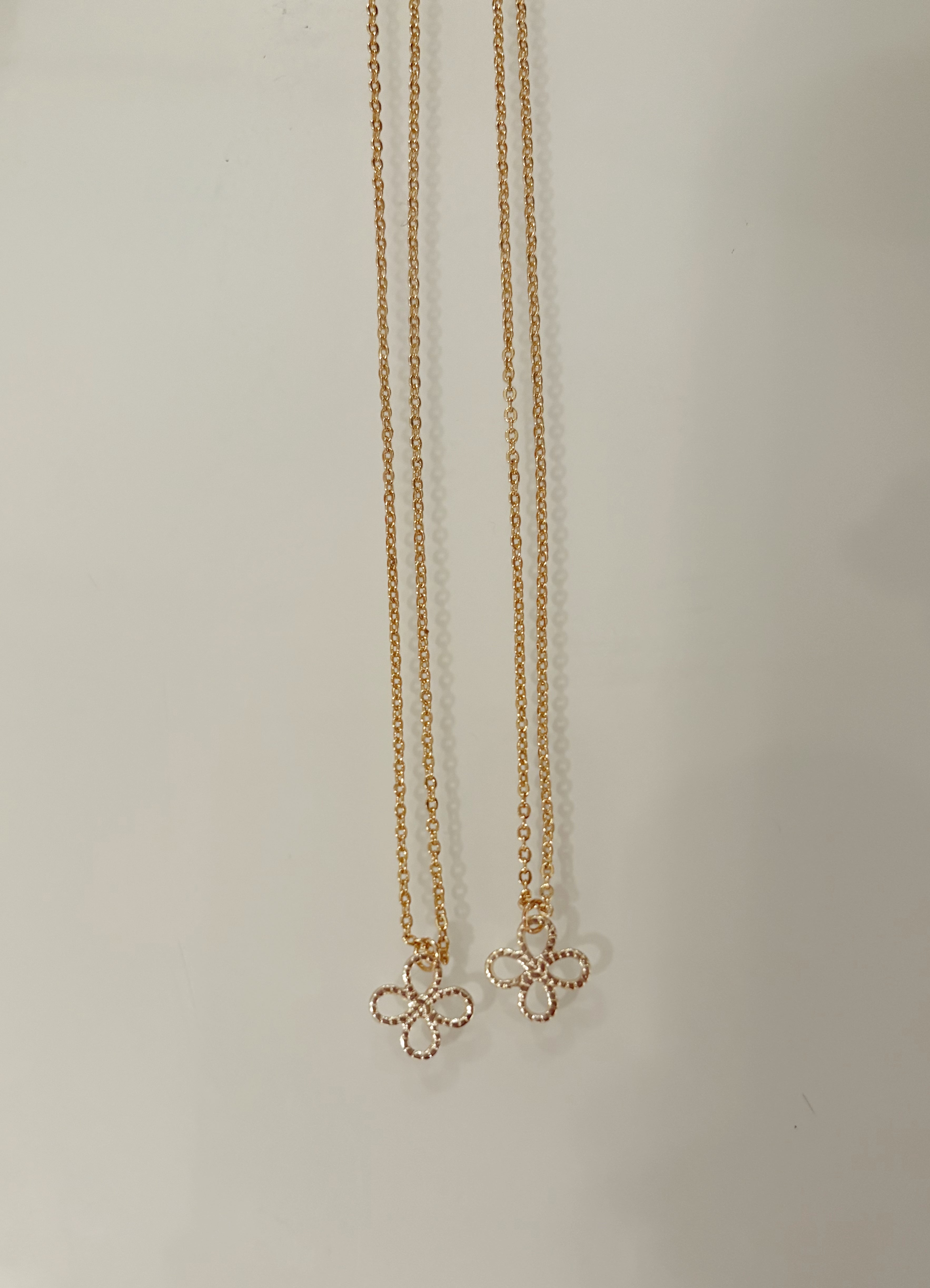 Two matching gold filled necklaces with floral pendants on a light gray background